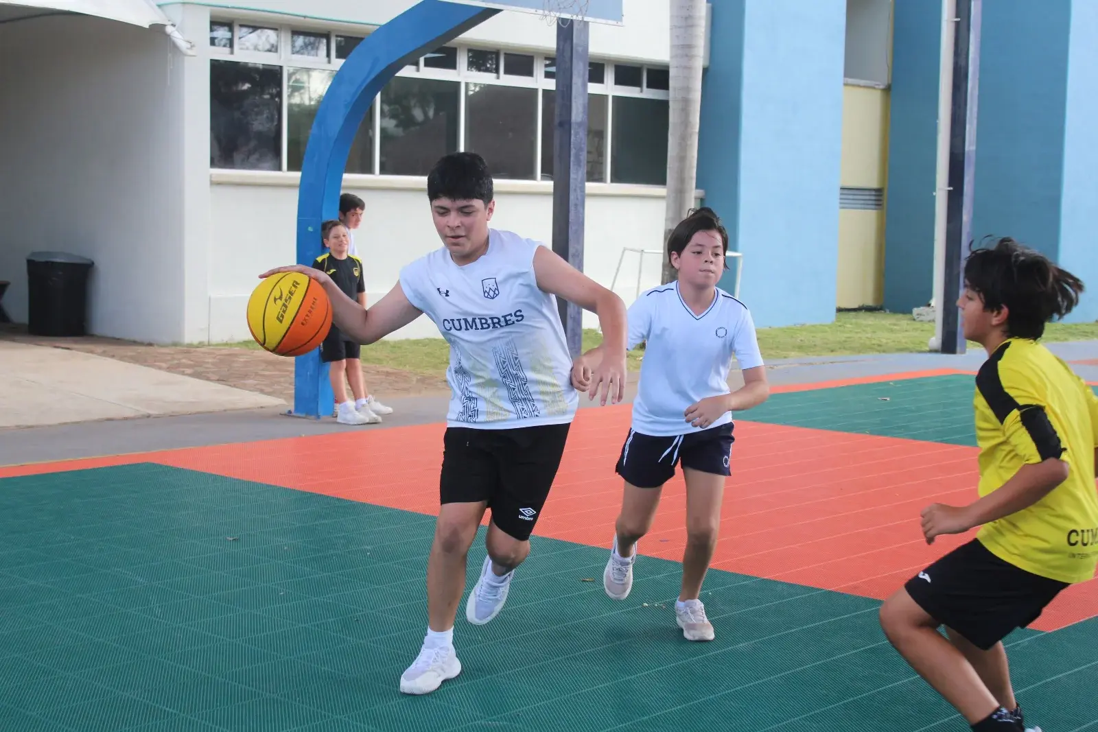 Estudiantes jugando baloncesto en la cancha deportiva del colegio durante actividad recreativa.